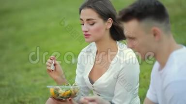 年轻夫妇坐在草地上吃沙拉，一起野餐